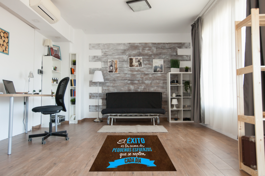 Sala moderna con sofá negro, escritorio, estantería y una alfombra decorativa en el suelo.