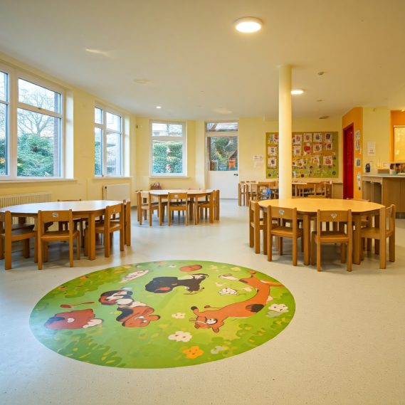 Aula luminosa con mesas de madera y una alfombra verde con animales.